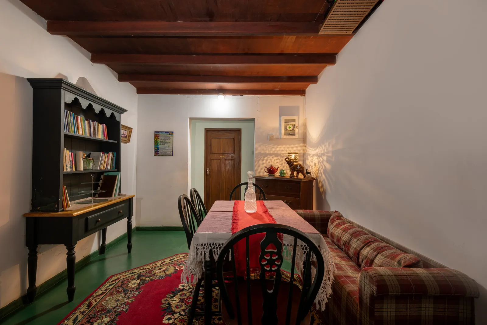The library: a dark dresser of books, a long table and a tartan sofa